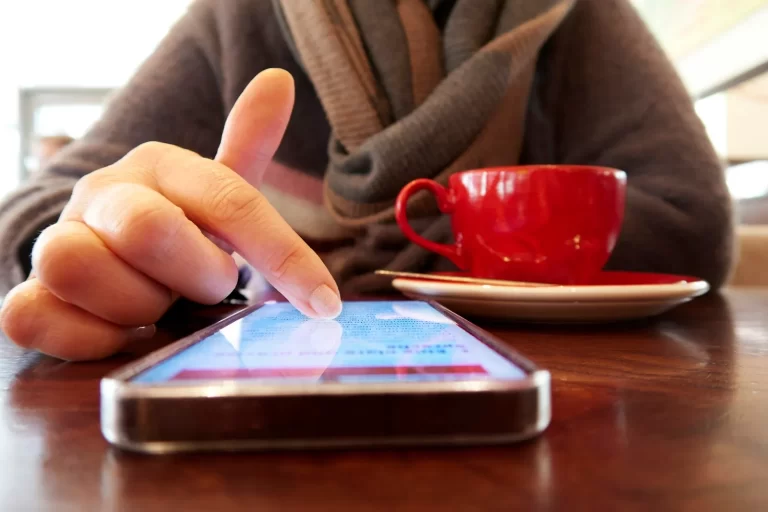 Persona tocando la pantalla de un móvil en la mesa de una cafetería